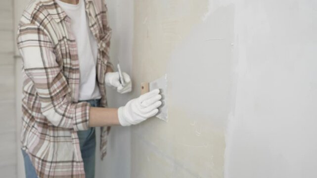 Unknown female construction worker wearing protective gloves applying plaster, smoothing wall surface during home renovation work