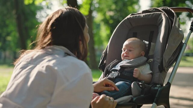 A beautiful young mother talks and laughs with her newborn baby sitting on the walkway in the park. Concept of education, family, happiness