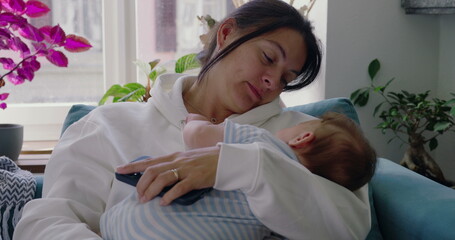 Mother holding her baby, gently resting on the couch, while the baby touches her face, candid...