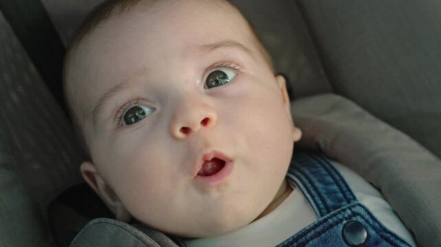 Close-up portrait of a newborn baby with light eyes, laughing and happy. The child is sitting in the stroller while walking with his family in the park at sunset
