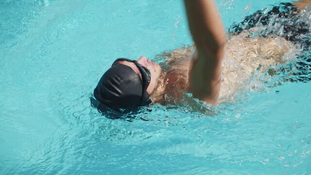 Professional swimmer swims in an outdoor pool. Young man swimming in pool in backstroke style - Slow motion video. Young pro swimmer athlete conducts a training session. Healthy lifestyle  concept.