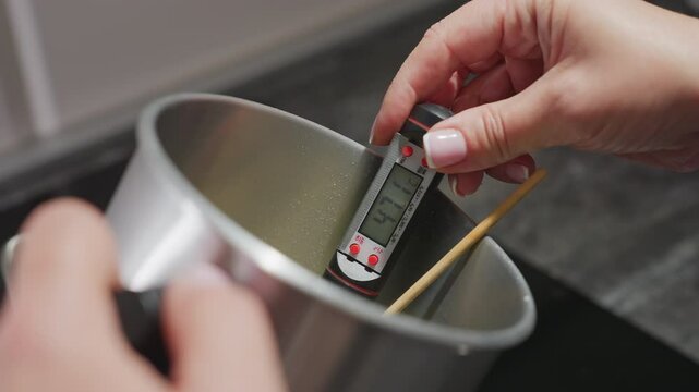 Closeup of hand holding digital food thermometer reading 47.4 degrees inside stainless mixing bowl with wooden turner, highlighting temperature accuracy and preparation process in kitchen environment