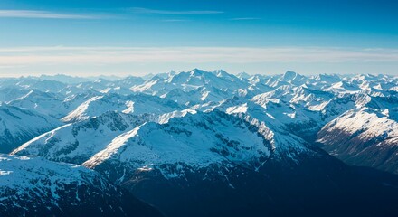 Aerial view of a vast mountain range covered in snow under a clear blue sky on a bright sunny day