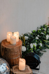 Romantic event setup with candles on tree trunks, disco ball, stage light, and floral arrangement for ambiance, casting soft light.