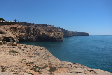 a photo of a rocky southern coast of portugal on a sunny summer day with ocean in the background
