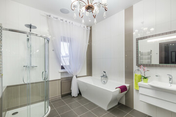 Exclusive bathroom design. Bath of original shape, window with drapery. Beautiful ceiling chandelier.