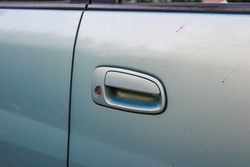 Close-up view of silver car door handle on light blue vehicle showing minimal design and smooth...