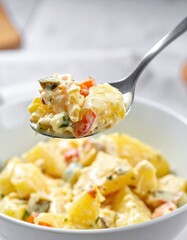 Close-up of creamy potato salad with vegetables on a spoon