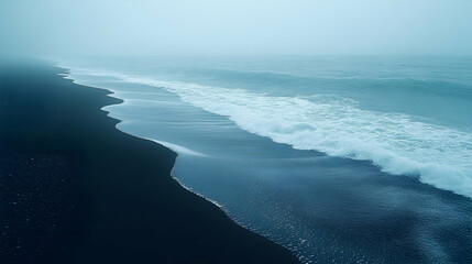 Misty black sand beach meets the ocean waves. Dark sand stretches to a misty ocean.  Waves crash gently