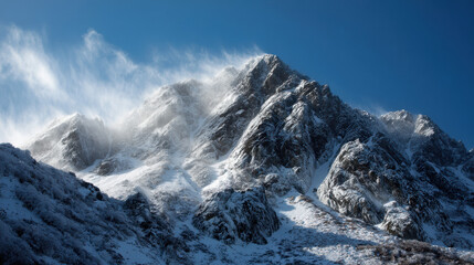 Majestic snow covered mountain peaks rise against a bright blue sky with wind blowing snow, showcasing the rugged beauty of nature's stunning landscape perfectly.