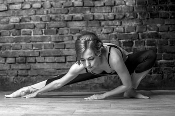 Young slender athletic girl in a turquoise tank top and dark leggings doing yoga against the background of a brick wall