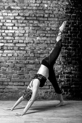 Young slender athletic girl in a turquoise tank top and dark leggings doing yoga against the background of a brick wall