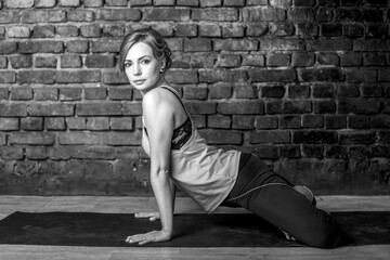 Young slender athletic girl in a turquoise tank top and dark leggings doing yoga against the background of a brick wall