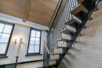 Wooden staircase with wrought iron railings against a white brick wall, in the interior of a...