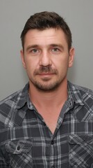 Fototapeta premium Portrait of a man in a checked shirt with a neutral expression against a gray background