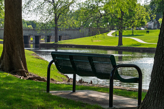 Empty park bench overlooking a calm pond and stone bridge