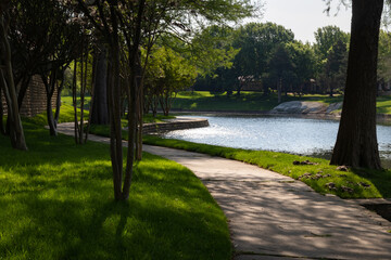 Winding Concrete Path Along a Peaceful Pond in a Sunlit Public Park