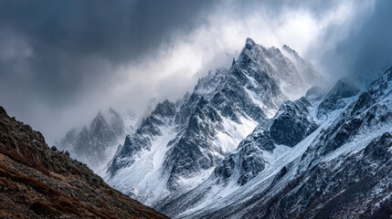 A dramatic view of snow covered mountain peaks piercing through swirling clouds and mist, creating an awe inspi and majestic alpine landscape scene.