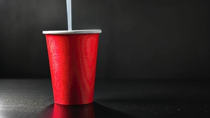 Red cup with a straw: A vibrant red cup with a silver rim, captures the eye with its bold simplicity, accompanied by a straw against a dark background, suggesting refreshment. 