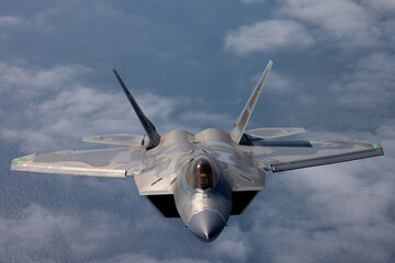 Frontal view of a a F-22 Raptor  flying over the Pacific ocean and a cloud layer 