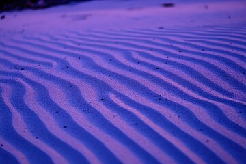 Fototapeta premium Close-up of rippled sand, purple hues. Detailed patterns of wind-formed dunes
