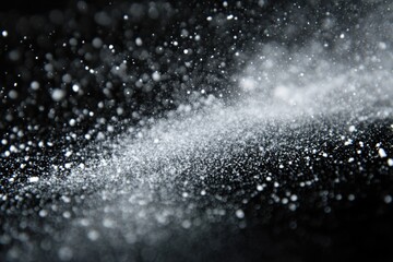 An abstract close-up shot of particles in motion, suggesting snow, dust, or other fine matter against a dark background.