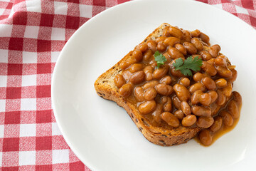 Baked beans on toast with white plate and checkered table cloth.
