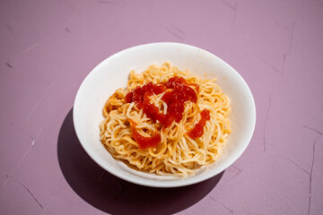 Squeezing ketchup on noodles in white bowl in close-up
