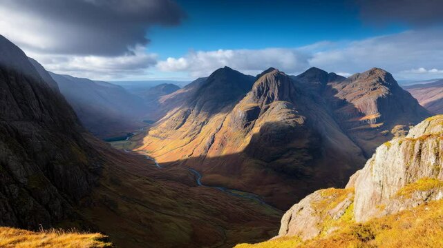 Scenic mountain valley with rugged peaks, winding river, rocky terrain, and patches of sunlight, creating a dramatic landscape view.