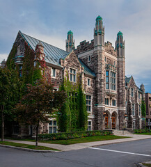 Elegant historic stone building with ivy-covered walls and green towers, photographed on a quiet street at sunset. Beautiful example of Gothic Revival architecture in an urban setting.