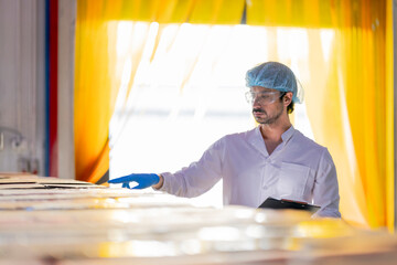 Food industry worker wearing hygiene gear inspects packaged products in a factory warehouse with...