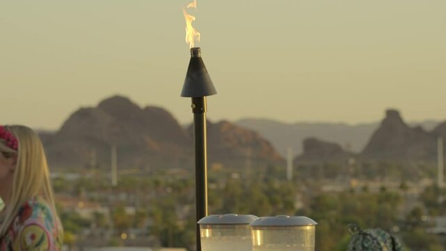 This video shows a tiki torch burning on a rooftop lounge at sunset, with a breathtaking mountain landscape in the background. 