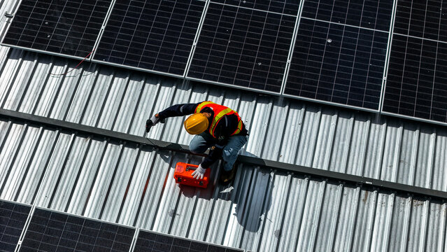 A worker wearing safety gear installing solar panels on a rooftop with nearby housing units in the background, emphasizing renewable energy, sustainability, and efficient solar power implementation