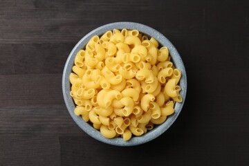 Raw horns pasta in bowl on dark wooden table, top view.