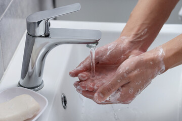 Woman washing her hands with foaming soap above sink in bathroom, closeup