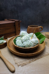 Traditional Asian dessert called klepon, sweet glutinous rice balls filled with melted palm sugar and coated with grated coconut in a wooden bowl with a natural background. Ideal for traditional food
