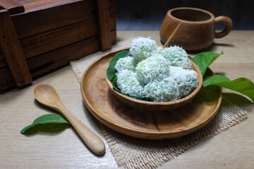 Traditional Asian dessert called klepon, sweet glutinous rice balls filled with melted palm sugar and coated with grated coconut in a wooden bowl with a natural background. Ideal for traditional food