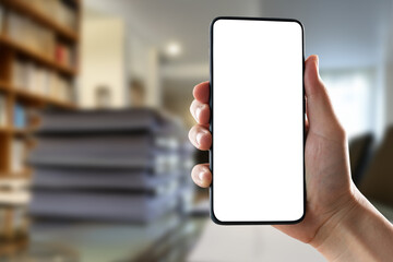 Modern smartphone held in hand with blank screen, stacks of documents in background, minimalistic workspace setting, perfect for display, technology and business use. Agnostic