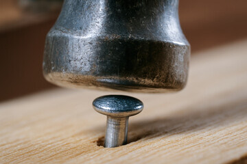 Hammer hitting nail on woodwork in workshop creating close up view of metal and wood textures with natural light