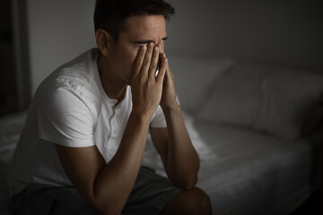 Young man feeling tired emotional stressed sitting on bed, mental health concept 