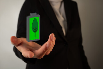 businesswoman's hand holding a 3D icon of a battery with a leaf in the center