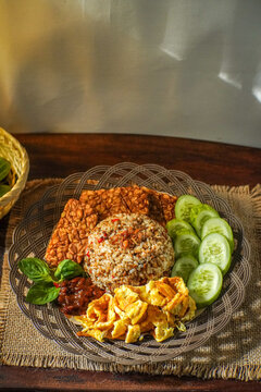 Traditional Sundanese dish "Nasi Tutug Oncom" served with tempeh, scrambled eggs, sambal, fresh cucumber slices, and basil. Rich in flavor, perfect for a hearty Indonesian breakfast.
