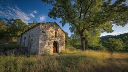 Obraz premium Ancient Stone House under the Green Tree: An antique stone house stands peacefully beneath the shade of a large green tree, the image evokes a sense of history and tranquility. 