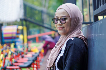 A joyful asian woman in a hijab laughs while adjusting her sunglasses, enjoying a relaxing moment