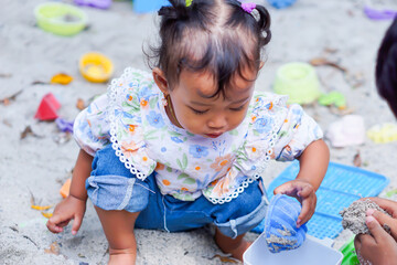 A little asian girl plays in the sand with toys, scooping and building happily at the playground.