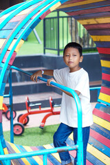A cheerful asian boy explores a colorful tunnel at the playground, enjoying a fun and active day out.