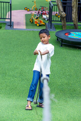 An asian boy plays tug of war with determination on green grass at a fun outdoor playground.