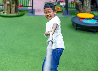 An asian boy plays tug of war with determination on green grass at a fun outdoor playground.