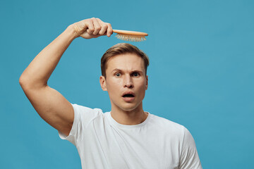surprised young caucasian man white t-shirt holding wooden hairbrush isolated on blue background hair loss concept male emotion care scalp