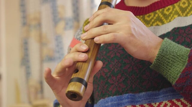 Close-up of a musician's hands playing a wooden flute Quena. The focus is on the intricate finger placement and the delicate interaction between the musician and the instrument. 